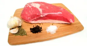 raw tri-tip steal on a wooden cutting boards surrounded by herbs